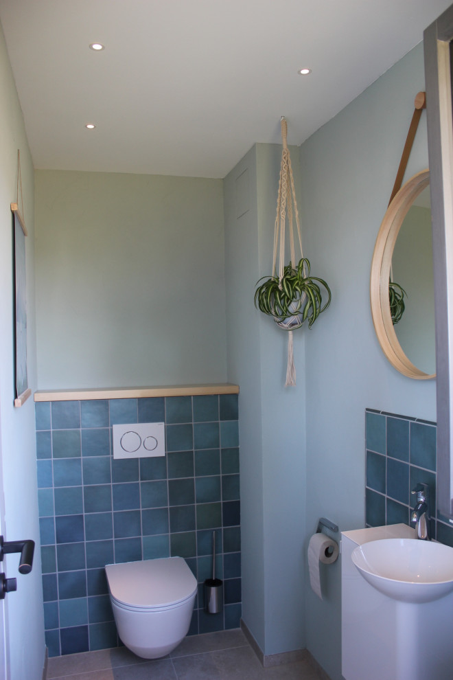 Small mediterranean cloakroom in Munich with a wall mounted toilet, blue tiles, ceramic tiles, blue walls, ceramic flooring, a wall-mounted sink, beige floors and a floating vanity unit.