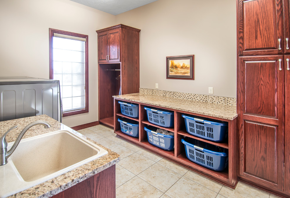 Inspiration for a mid-sized transitional galley dedicated laundry room in Omaha with a single-bowl sink, raised-panel cabinets, dark wood cabinets, granite benchtops, beige walls, ceramic floors and a side-by-side washer and dryer.