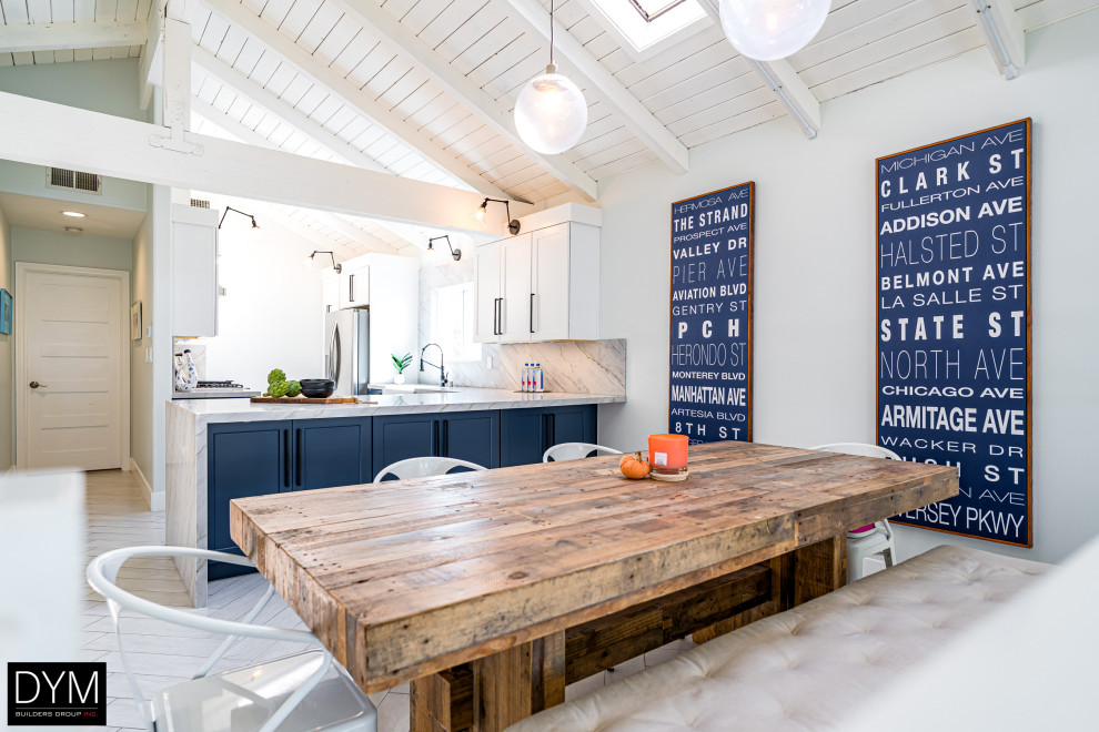 Beach style galley white floor, vaulted ceiling and light wood floor eat-in kitchen photo in Los Angeles with a farmhouse sink, shaker cabinets, blue cabinets, quartz countertops, white backsplash, quartz backsplash, stainless steel appliances, a peninsula and white countertops