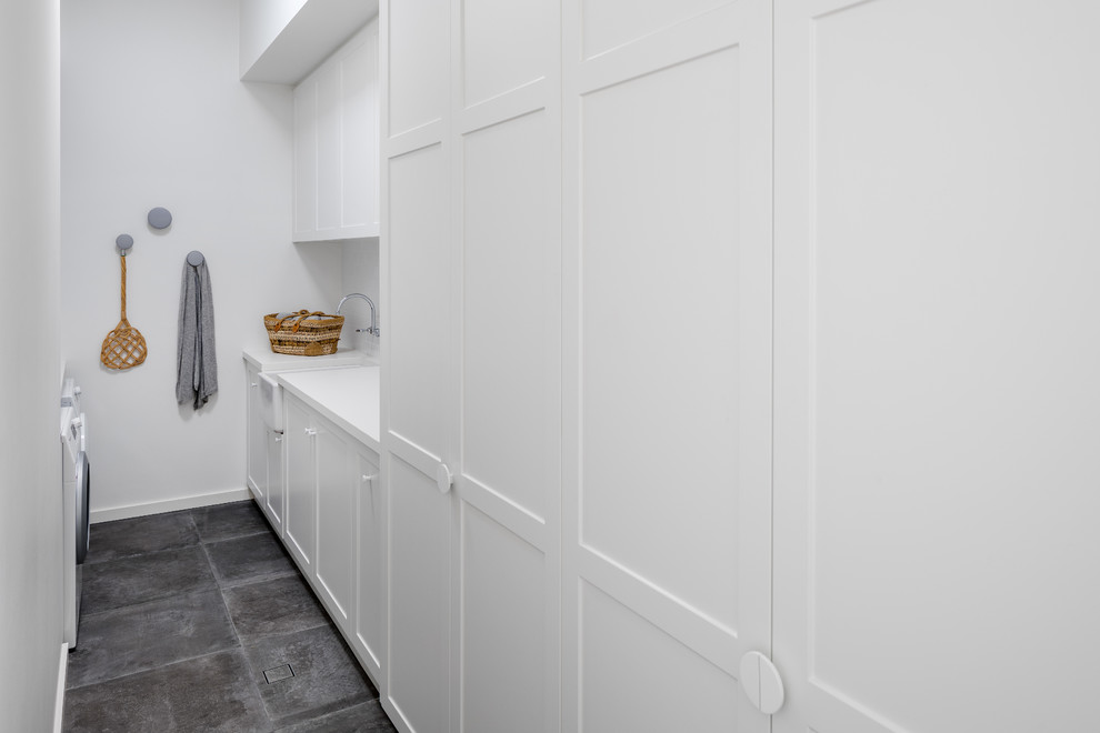 Mid-sized contemporary galley utility room in Perth with a farmhouse sink, shaker cabinets, white cabinets, quartz benchtops, white walls, porcelain floors, a side-by-side washer and dryer, grey floor and white benchtop.