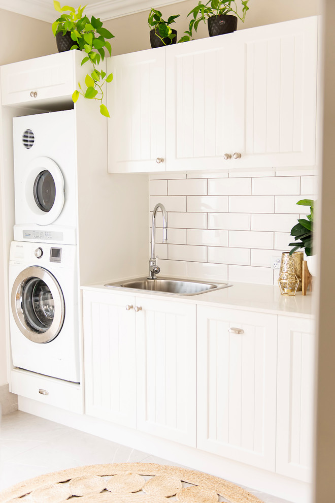 Design ideas for a large traditional l-shaped laundry room in Brisbane with shaker cabinets, white cabinets, quartz benchtops, beige walls, porcelain floors, a stacked washer and dryer, grey floor and white benchtop.