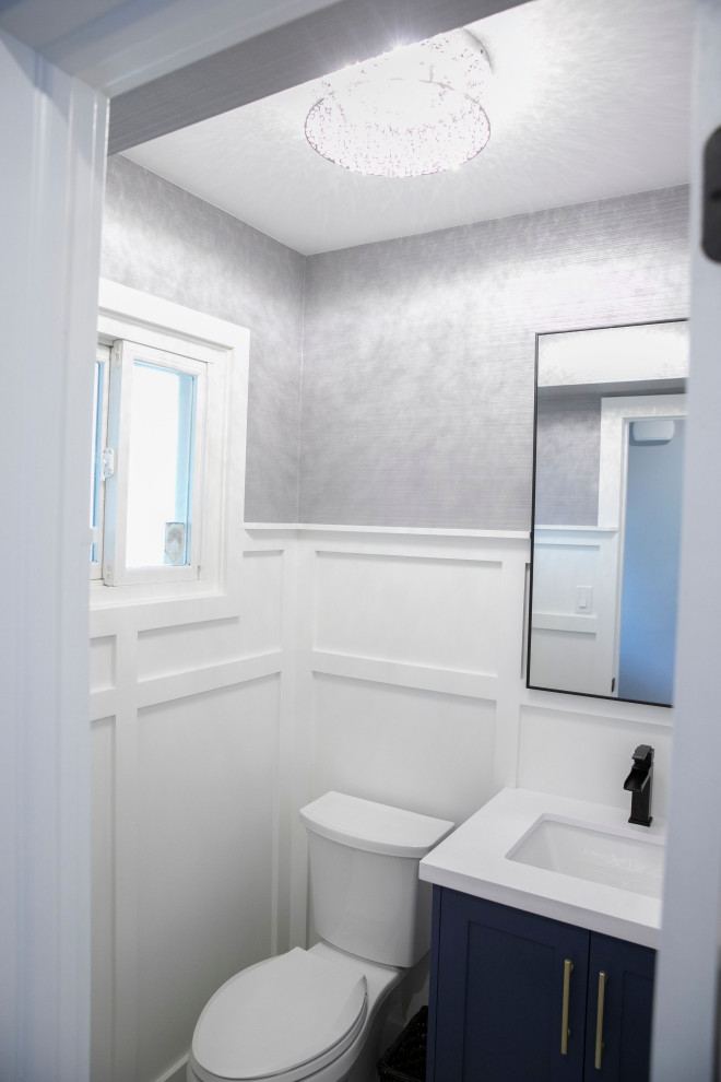Small contemporary powder room in Toronto with recessed-panel cabinets, blue cabinets, a one-piece toilet, ceramic floors, an undermount sink, engineered quartz benchtops, multi-coloured floor, white benchtops, a built-in vanity and decorative wall panelling.