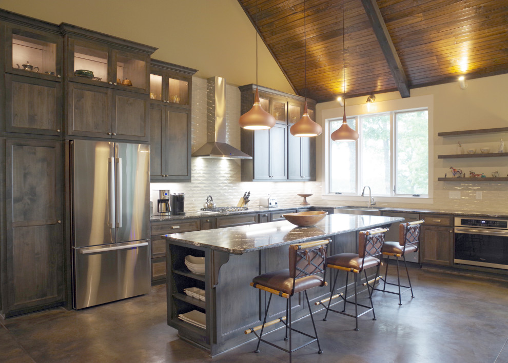 Photo of a l-shaped open plan kitchen in Nashville with shaker cabinets, dark wood cabinets, porcelain splashback, stainless steel appliances, concrete floors, with island, black benchtop and vaulted.