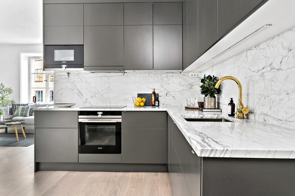 Inspiration for an expansive contemporary l-shaped kitchen in Stockholm with an undermount sink, flat-panel cabinets, grey cabinets, white splashback, stone slab splashback, black appliances, light hardwood floors and no island.