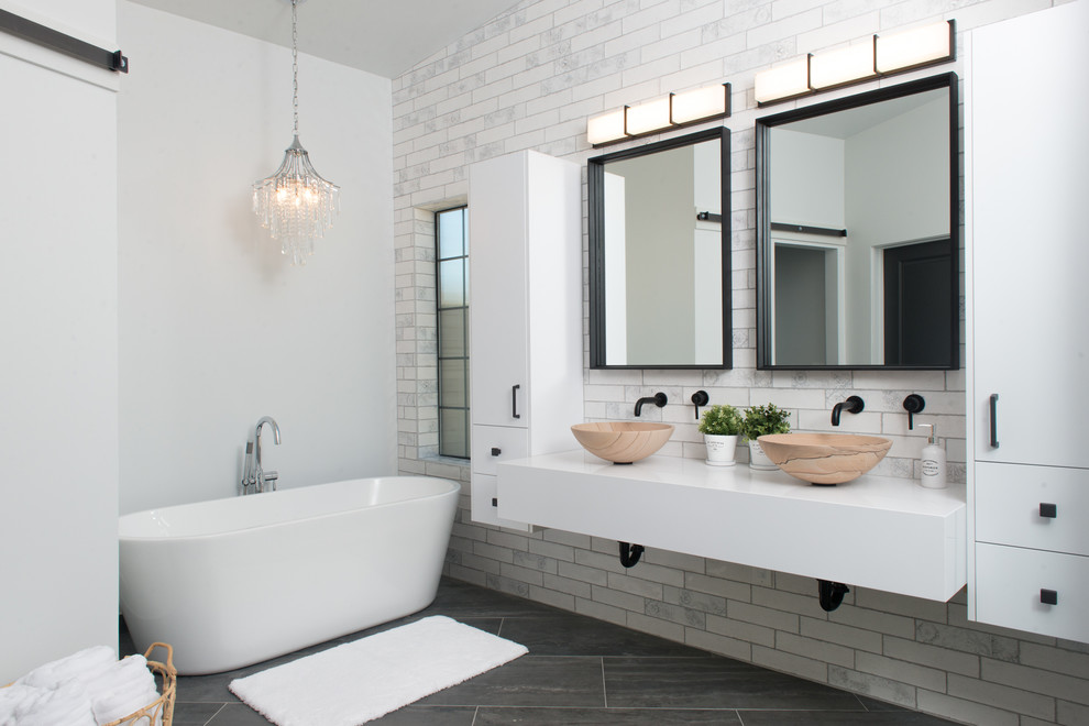 Inspiration for a mid-sized industrial master bathroom in Phoenix with flat-panel cabinets, white cabinets, a freestanding tub, a curbless shower, a one-piece toilet, white tile, ceramic tile, white walls, ceramic floors, a vessel sink, quartzite benchtops, grey floor, a hinged shower door and white benchtops.