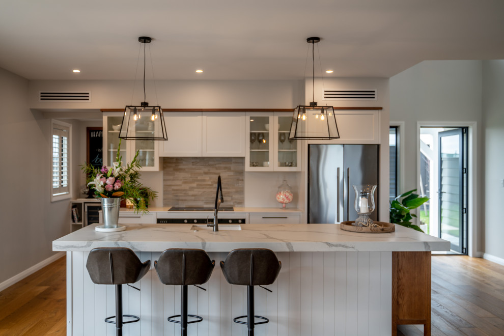 Inspiration for a large country single-wall eat-in kitchen in Auckland with an undermount sink, shaker cabinets, white cabinets, quartzite benchtops, grey splashback, mosaic tile splashback, stainless steel appliances, medium hardwood floors, with island, brown floor, white benchtop and vaulted.