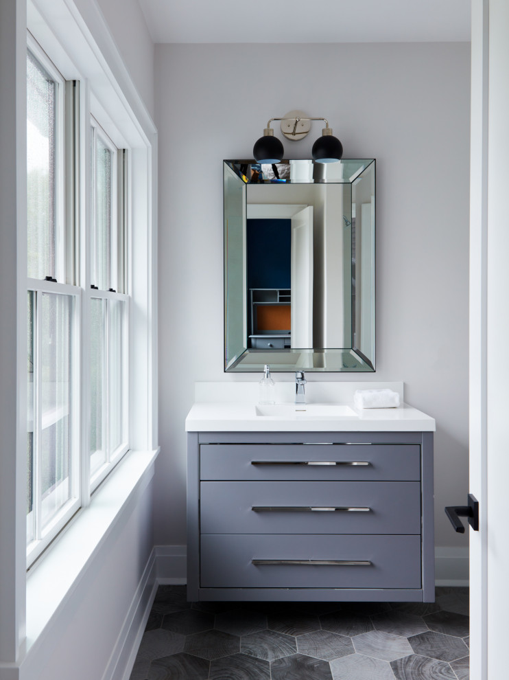 This is an example of a small transitional powder room in New York with grey cabinets, grey walls, porcelain floors, an integrated sink, engineered quartz benchtops, black floor, white benchtops, a floating vanity and a two-piece toilet.