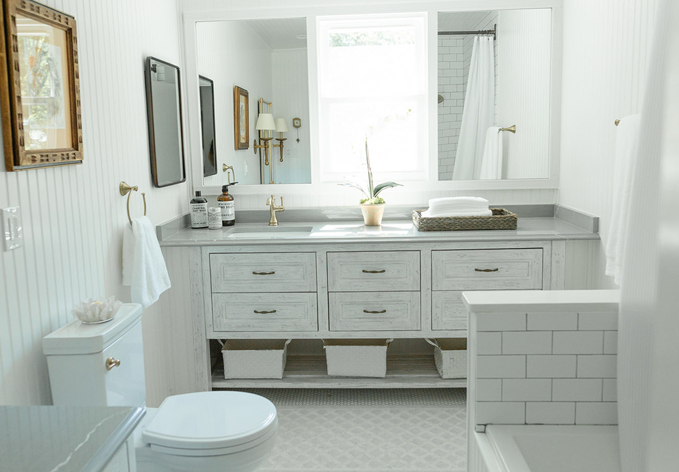 Inspiration for a mid-sized transitional master bathroom in Columbus with beaded inset cabinets, grey cabinets, a drop-in tub, a shower/bathtub combo, a two-piece toilet, white tile, subway tile, white walls, mosaic tile floors, a drop-in sink, quartzite benchtops, white floor and a shower curtain.