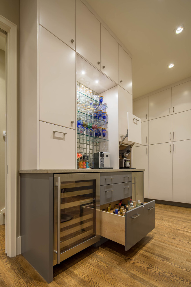 Photo of a mid-sized modern single-wall wet bar in Austin with no sink, flat-panel cabinets, grey cabinets, quartz benchtops, glass tile splashback and light hardwood floors.