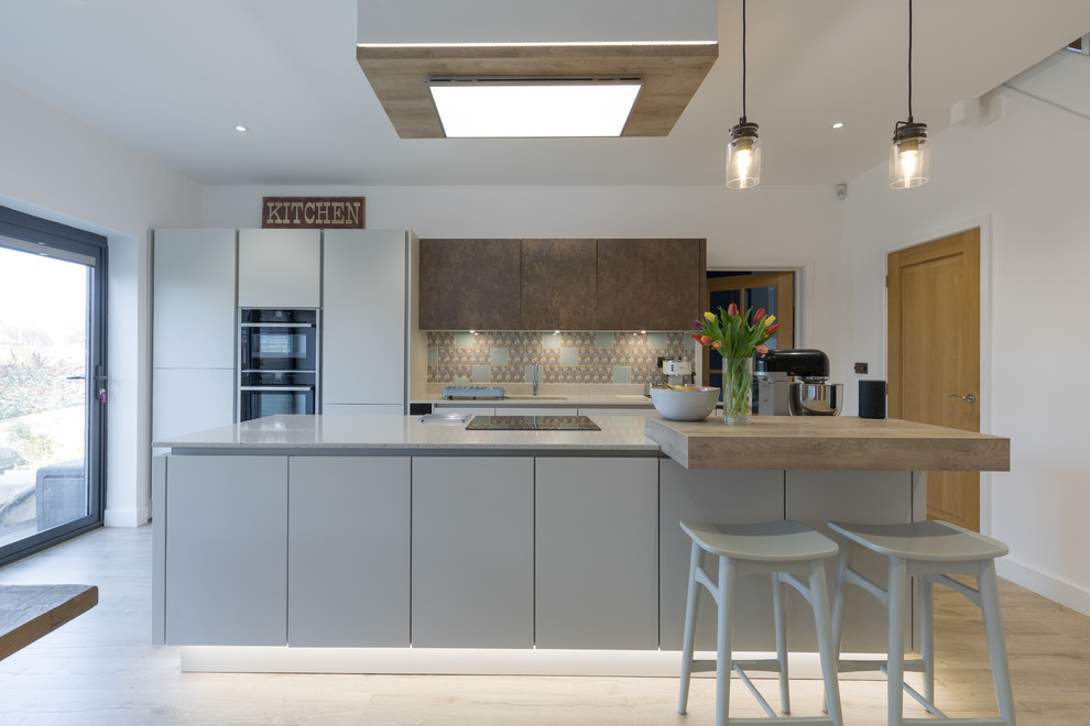 Design ideas for a mid-sized modern single-wall open plan kitchen in Hampshire with an undermount sink, flat-panel cabinets, white cabinets, quartzite benchtops, metallic splashback, panelled appliances, light hardwood floors and with island.