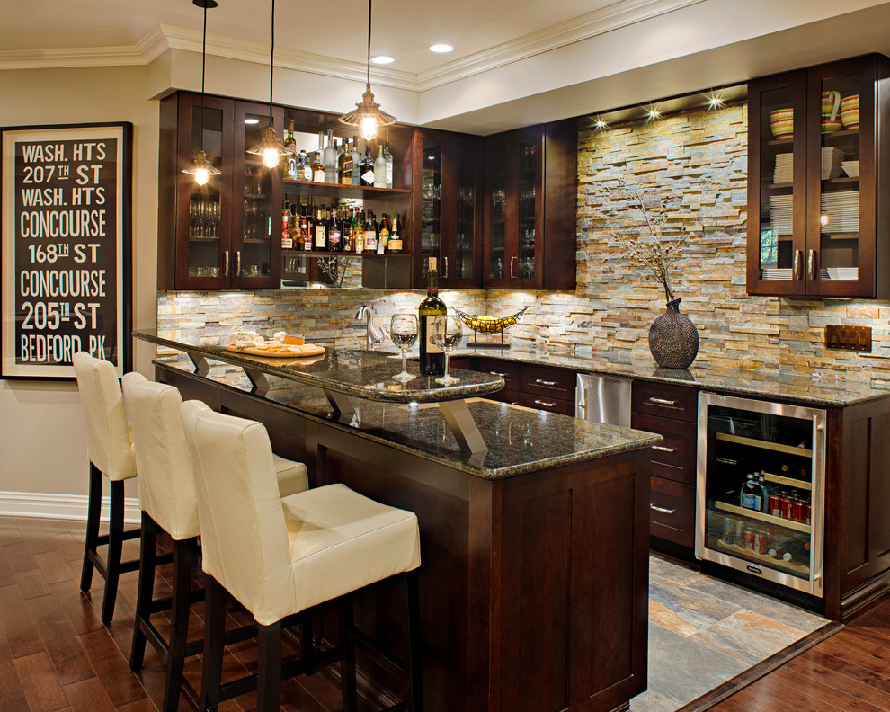 Photo of a large transitional u-shaped seated home bar in New York with dark hardwood floors, glass-front cabinets, dark wood cabinets, multi-coloured splashback, stone tile splashback, grey benchtop and granite benchtops.