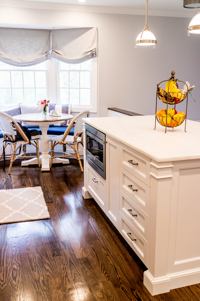 Mid-sized transitional dark wood floor and brown floor enclosed kitchen photo in New York with a farmhouse sink, recessed-panel cabinets, white cabinets, quartzite countertops, white backsplash, subway tile backsplash, stainless steel appliances and an island