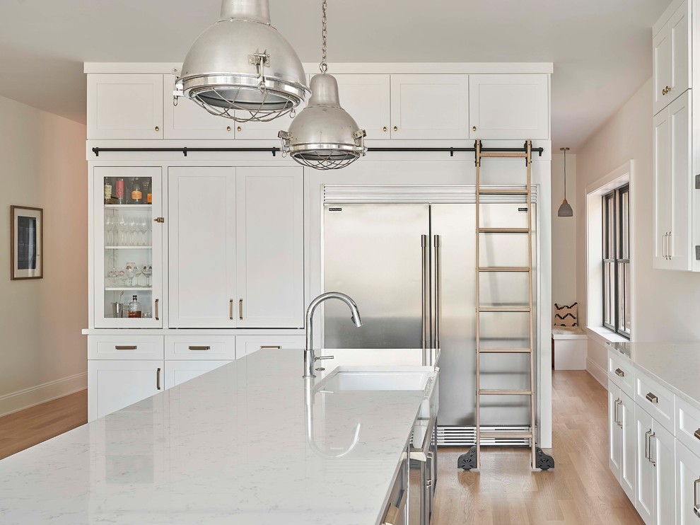 Design ideas for a mid-sized transitional single-wall eat-in kitchen in Chicago with a farmhouse sink, shaker cabinets, quartzite benchtops, white splashback, ceramic splashback, stainless steel appliances, light hardwood floors, with island and white benchtop.