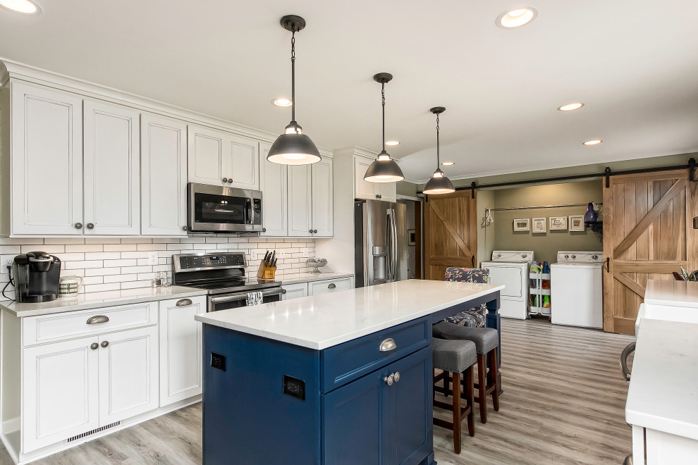 Large country kitchen in Columbus with a farmhouse sink, recessed-panel cabinets, white cabinets, quartzite benchtops, white splashback, stainless steel appliances, laminate floors, with island, grey floor and white benchtop.