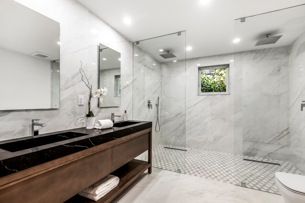 Inspiration for a large contemporary master bathroom in Miami with dark wood cabinets, a double shower, a one-piece toilet, white tile, marble, white walls, marble floors, marble benchtops, white floor, an open shower, black benchtops, a double vanity and a freestanding vanity.