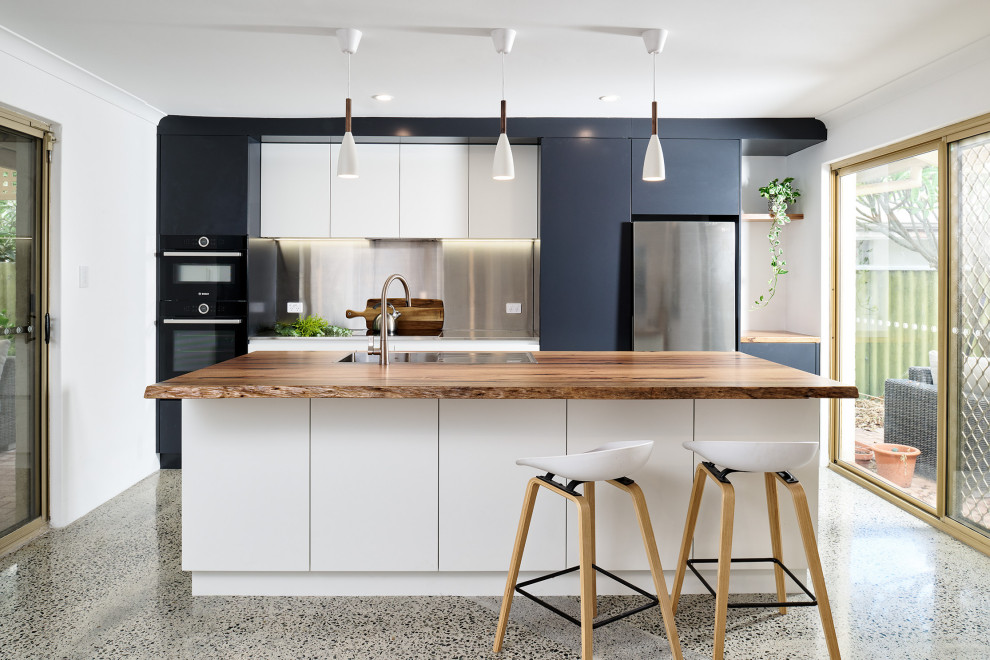Mid-sized industrial galley eat-in kitchen in Perth with a drop-in sink, flat-panel cabinets, black cabinets, stainless steel benchtops, grey splashback, black appliances, concrete floors, with island, grey floor and grey benchtop.