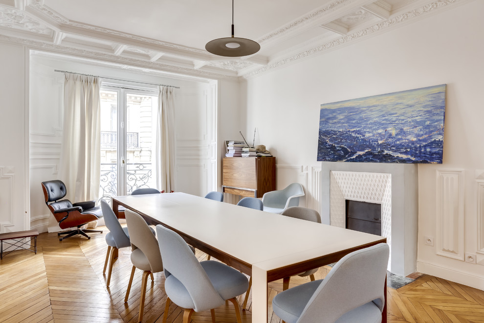 This is an example of a scandinavian dining room in Paris with white walls, medium hardwood floors and a standard fireplace.