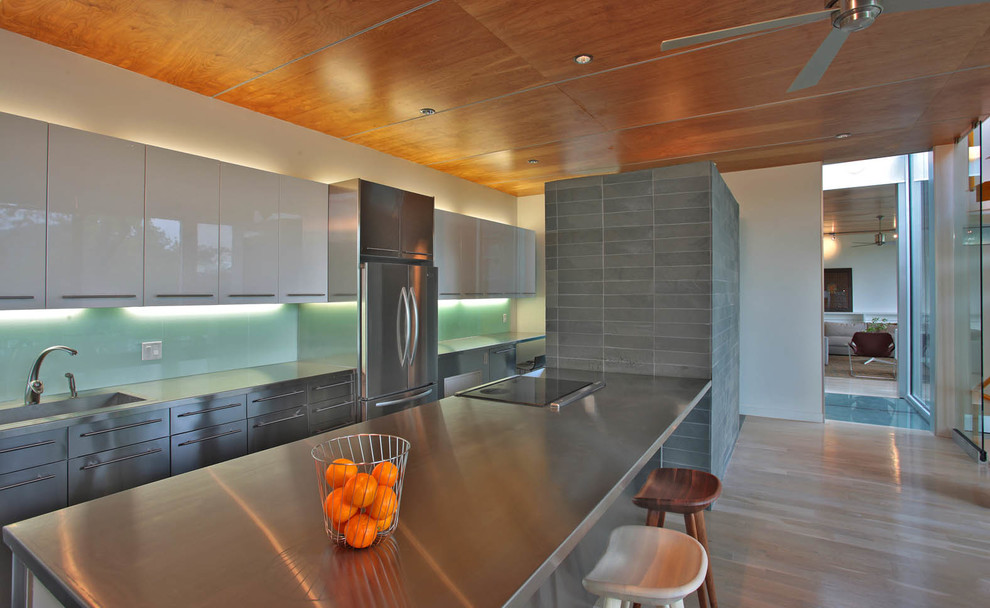 Photo of a modern galley kitchen in DC Metro with an integrated sink, flat-panel cabinets, stainless steel cabinets, stainless steel benchtops, glass sheet splashback and stainless steel appliances.