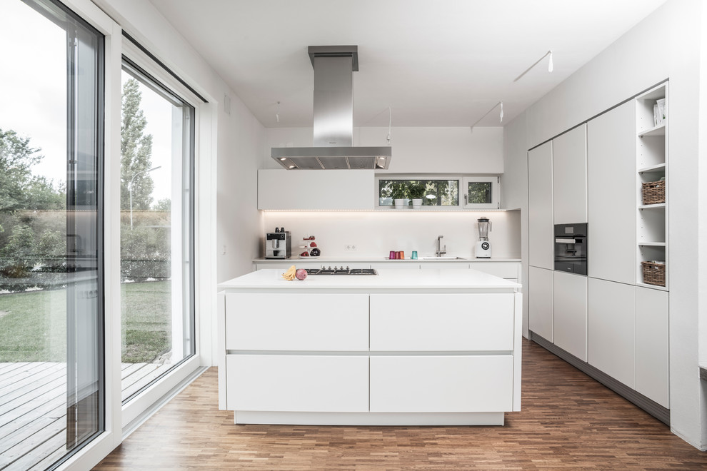 This is an example of a mid-sized contemporary l-shaped open plan kitchen in Other with flat-panel cabinets, white splashback, black appliances, dark hardwood floors, with island, brown floor and white cabinets.
