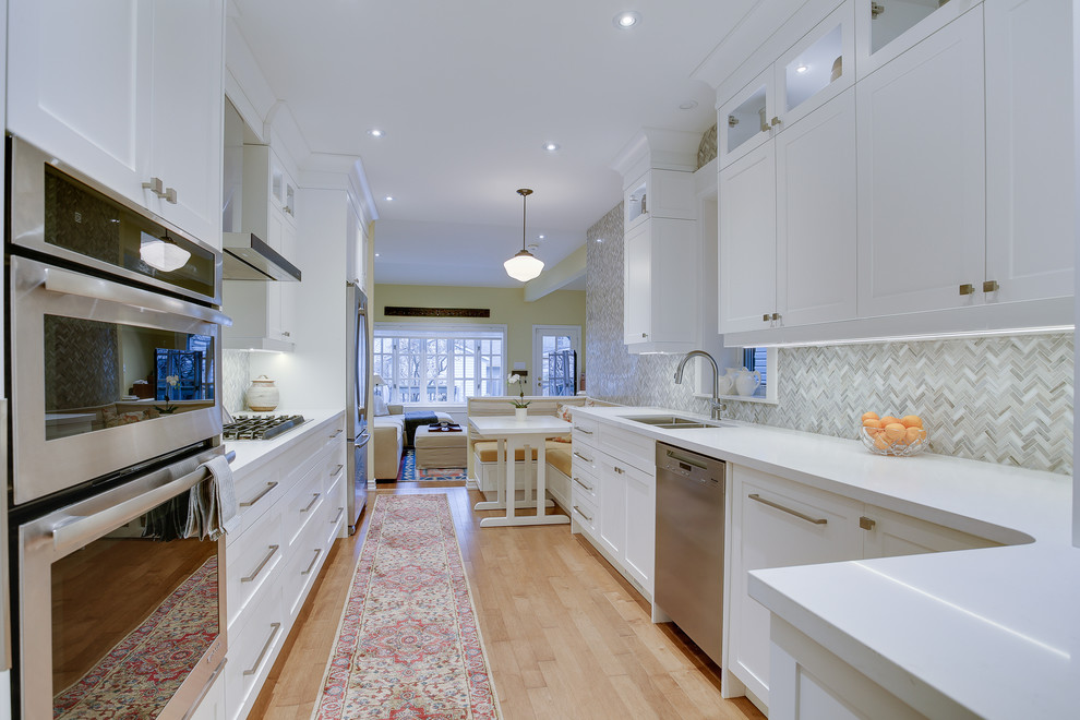 Inspiration for a mid-sized transitional galley kitchen in Toronto with an undermount sink, shaker cabinets, white cabinets, quartz benchtops, grey splashback, stone tile splashback, stainless steel appliances, medium hardwood floors and no island.