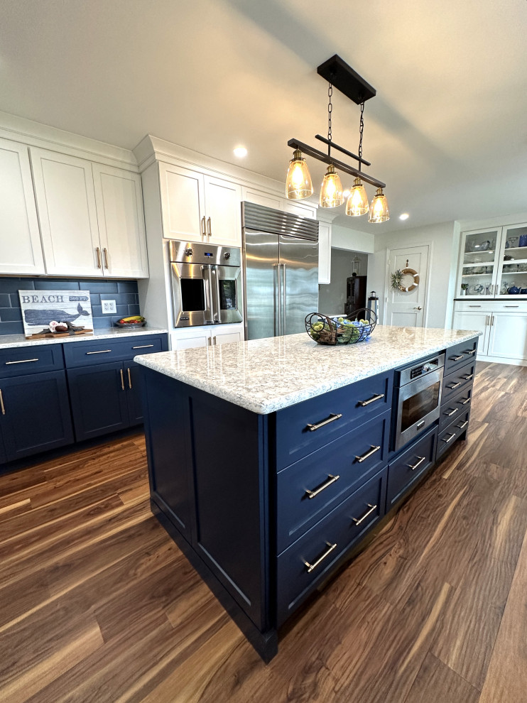 This is an example of a large transitional galley eat-in kitchen in Detroit with an undermount sink, shaker cabinets, white cabinets, quartz benchtops, blue splashback, ceramic splashback, stainless steel appliances, medium hardwood floors, with island, brown floor and white benchtop.