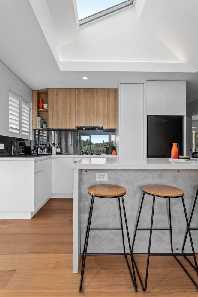 Mid-sized contemporary l-shaped open plan kitchen in Sydney with an undermount sink, flat-panel cabinets, white cabinets, quartz benchtops, metallic splashback, mirror splashback, stainless steel appliances, medium hardwood floors, with island, brown floor, white benchtop and vaulted.