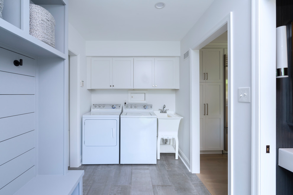 Photo of a small modern single-wall utility room in Philadelphia with an utility sink, shaker cabinets, white cabinets, white walls, ceramic floors, a side-by-side washer and dryer and grey floor.