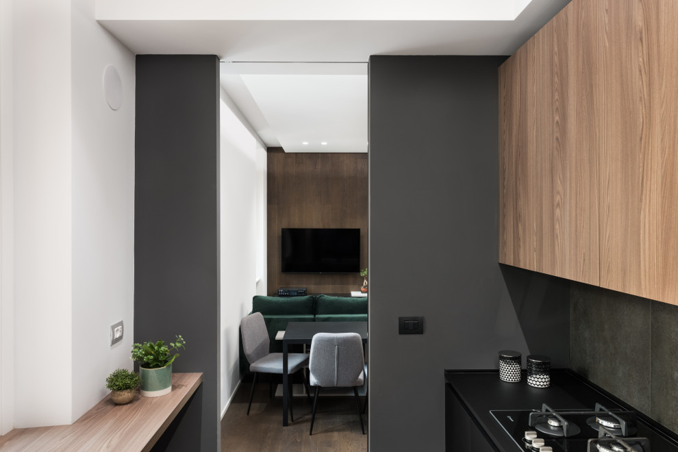 Small industrial l-shaped separate kitchen in Rome with a single-bowl sink, flat-panel cabinets, dark wood cabinets, solid surface benchtops, grey splashback, porcelain splashback, black appliances, porcelain floors, no island, grey floor, black benchtop and recessed.