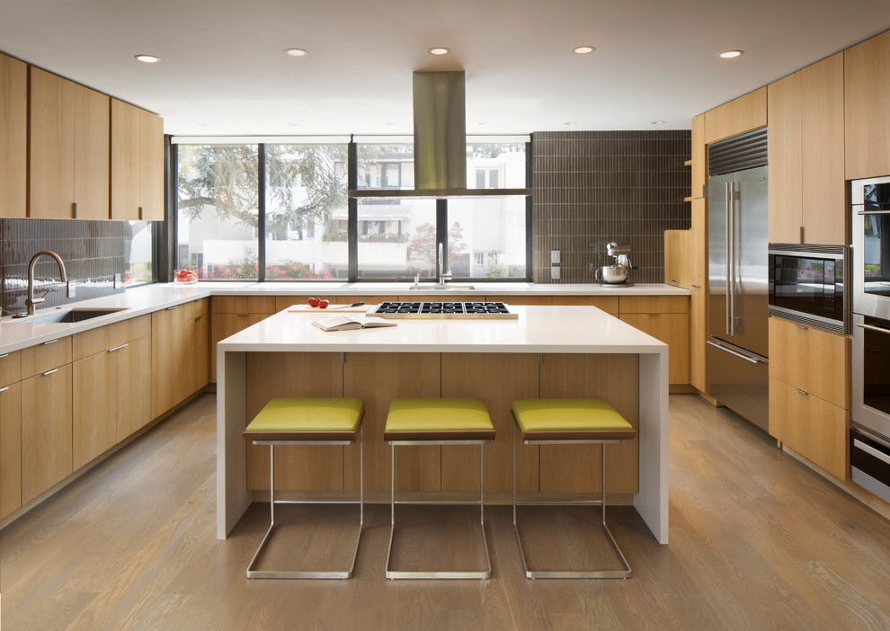 Design ideas for a midcentury kitchen in San Francisco with an undermount sink, flat-panel cabinets, light wood cabinets, quartz benchtops, glass tile splashback, stainless steel appliances, light hardwood floors, with island and brown splashback.