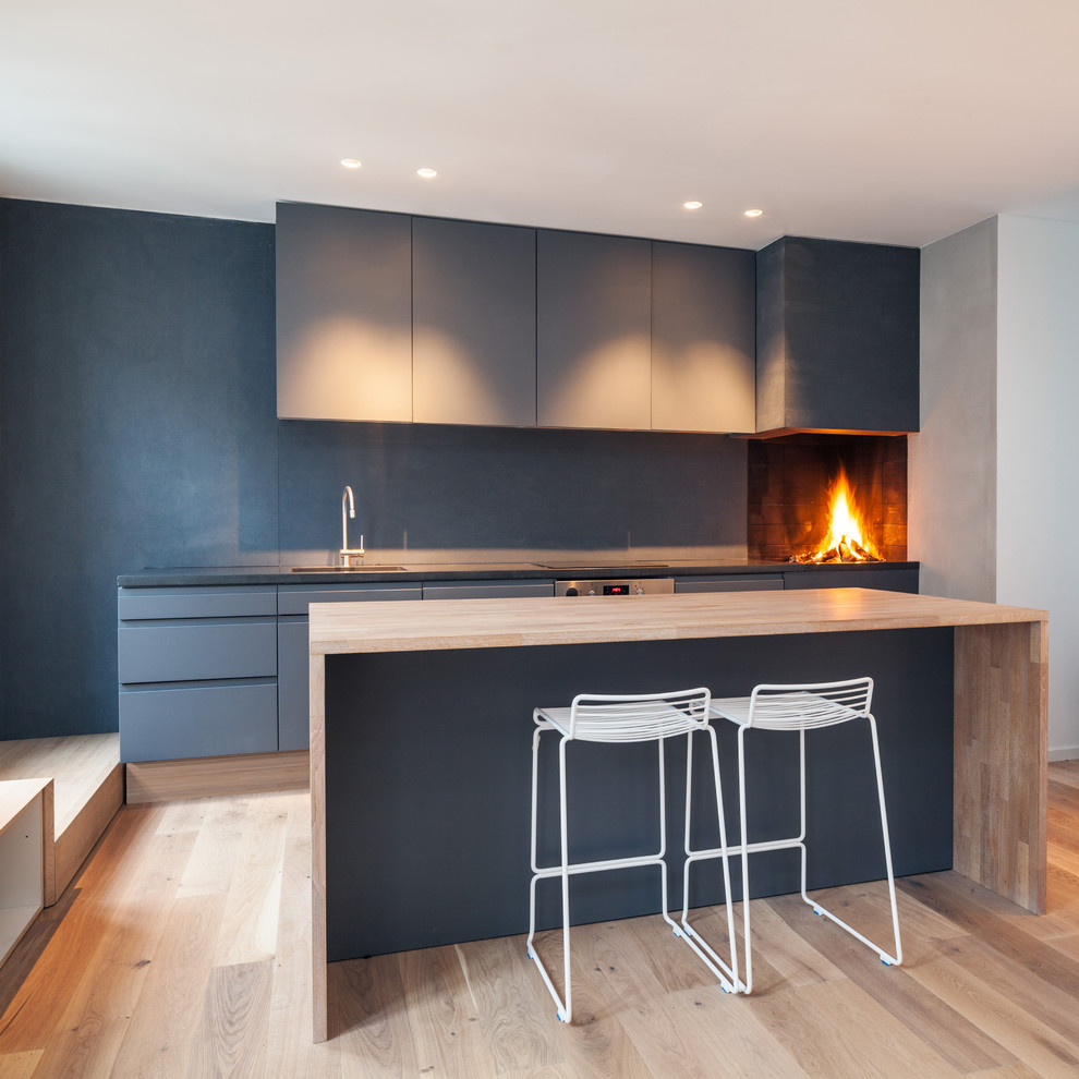 This is an example of a scandinavian single-wall kitchen in London with flat-panel cabinets, blue cabinets, wood benchtops, blue splashback, light hardwood floors and with island.