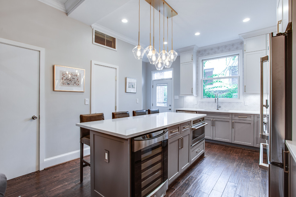 Example of a large transitional l-shaped medium tone wood floor and brown floor eat-in kitchen design in DC Metro with an undermount sink, shaker cabinets, white cabinets, solid surface countertops, white backsplash, ceramic backsplash, stainless steel appliances, an island and white countertops