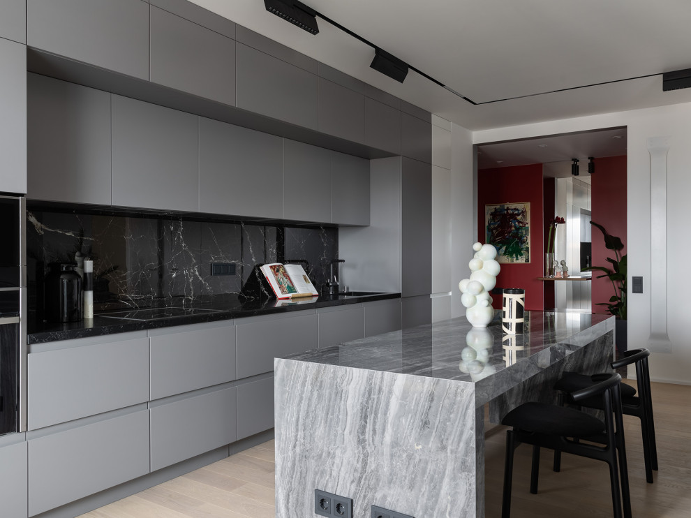 Inspiration for a contemporary open plan kitchen in Saint Petersburg with a single-bowl sink, flat-panel cabinets, grey cabinets, black splashback, light hardwood flooring, an island and black worktops.