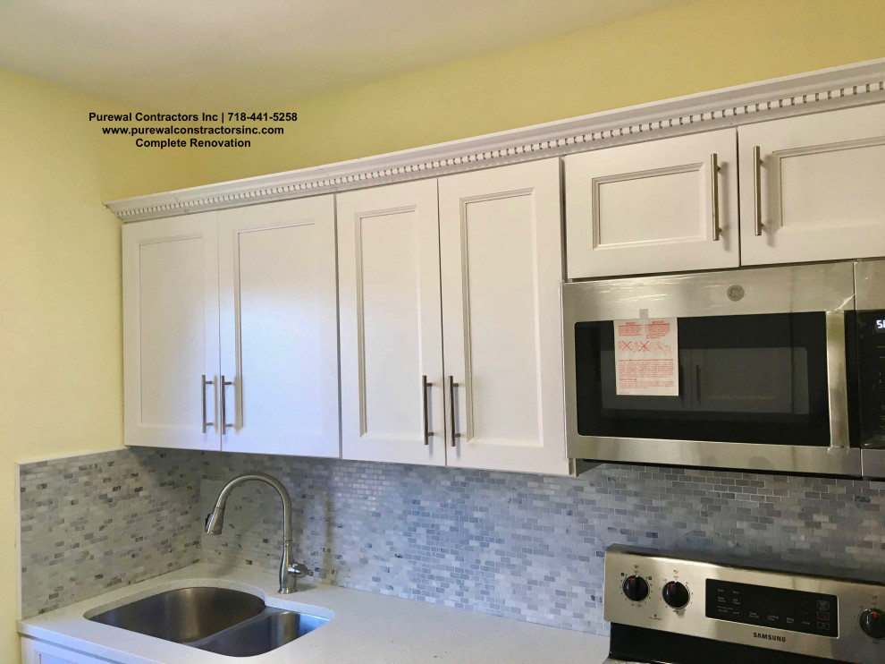 This is an example of a mid-sized galley separate kitchen in New York with a triple-bowl sink, raised-panel cabinets, white cabinets, quartz benchtops, grey splashback, mosaic tile splashback, black appliances, cement tiles, grey floor and white benchtop.