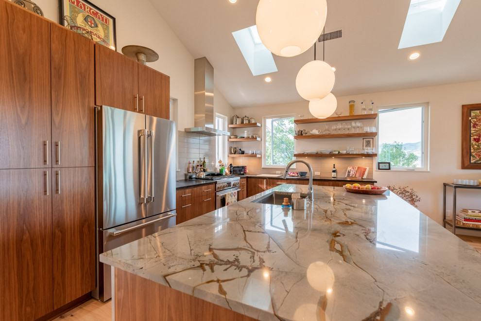 Photo of a large midcentury l-shaped open plan kitchen in Other with an undermount sink, flat-panel cabinets, medium wood cabinets, granite benchtops, grey splashback, glass tile splashback, stainless steel appliances, light hardwood floors, with island, brown floor, multi-coloured benchtop and vaulted.