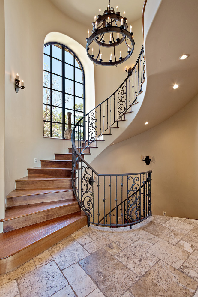 This is an example of a large mediterranean wood curved staircase in San Diego with wood risers and metal railing.