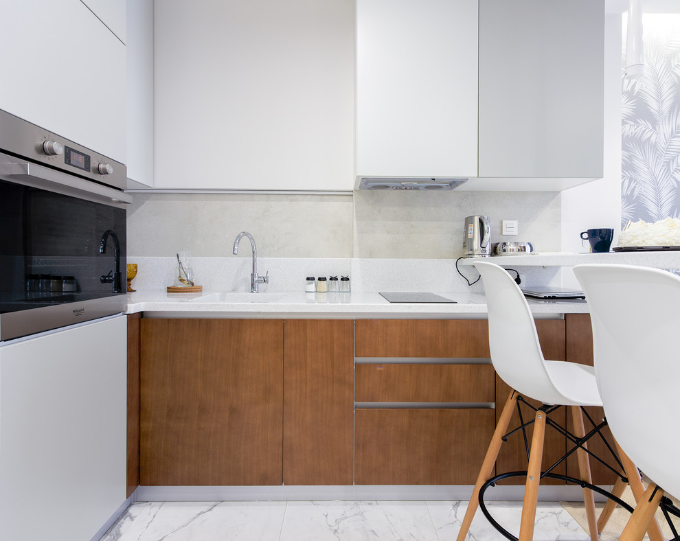 Photo of a small contemporary l-shaped open plan kitchen in Novosibirsk with an undermount sink, flat-panel cabinets, medium wood cabinets, solid surface benchtops, white splashback, stainless steel appliances, porcelain floors, a peninsula, white floor and white benchtop.
