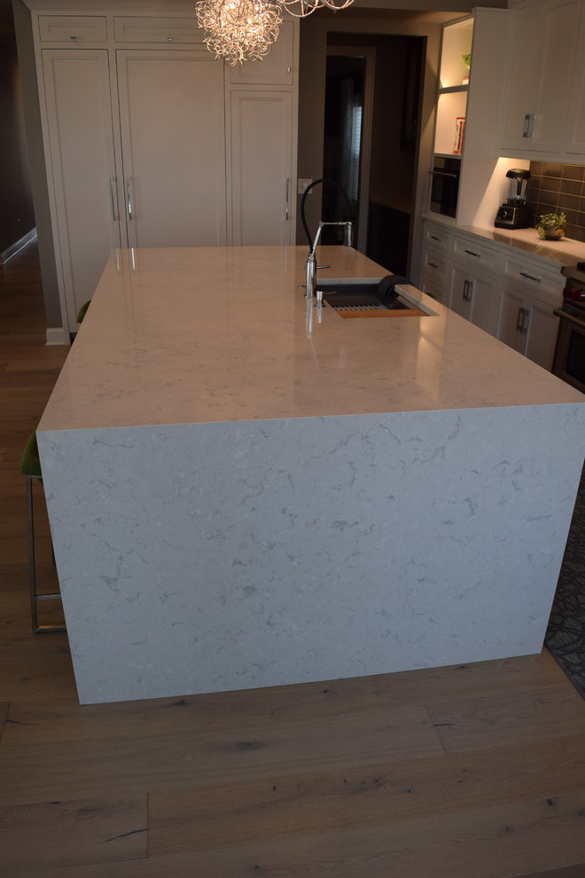 Example of a large transitional l-shaped light wood floor and multicolored floor eat-in kitchen design in Chicago with beaded inset cabinets, white cabinets, quartz countertops, black backsplash, ceramic backsplash, stainless steel appliances and an island