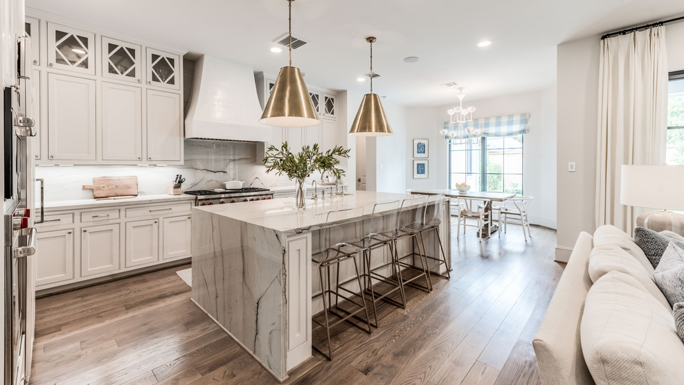 This is an example of a transitional l-shaped eat-in kitchen in Houston with a farmhouse sink, shaker cabinets, white cabinets, grey splashback, stainless steel appliances, medium hardwood floors, with island, brown floor and grey benchtop.