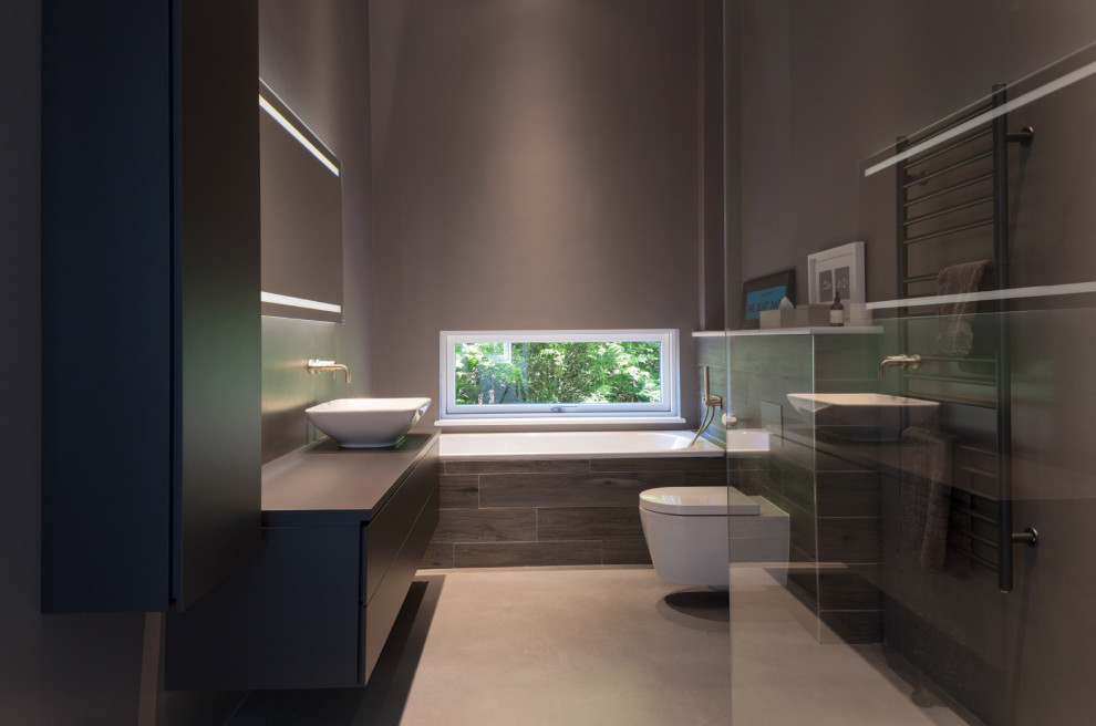 Photo of a mid-sized contemporary master bathroom in Oxfordshire with flat-panel cabinets, black cabinets, a drop-in tub, a corner shower, gray tile, porcelain tile, grey walls, porcelain floors, a vessel sink, grey floor, black benchtops, a single vanity and a built-in vanity.