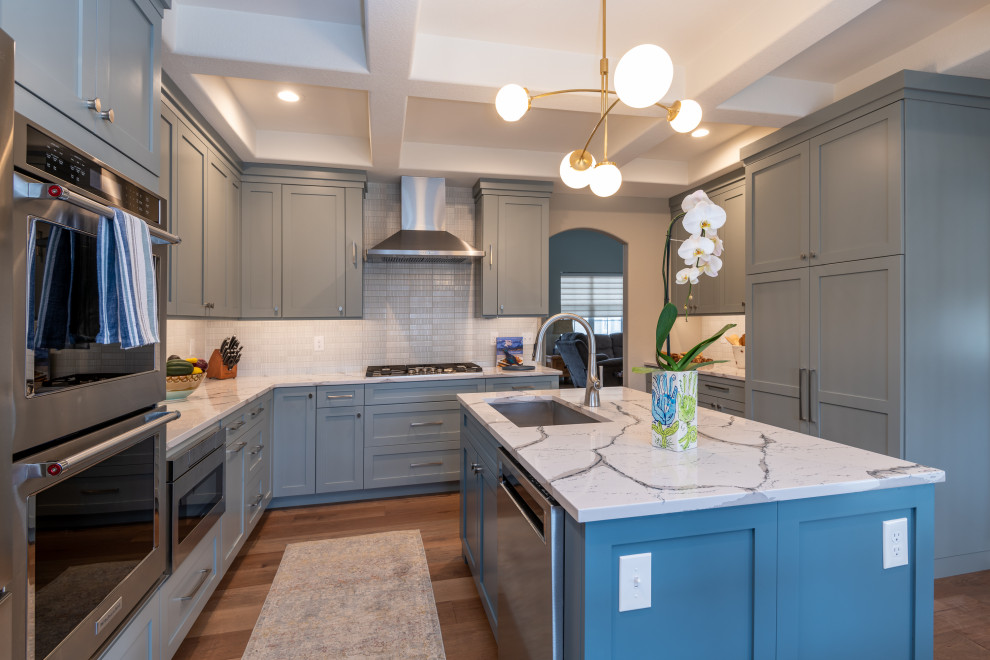 Mid-sized transitional u-shaped laminate floor, brown floor and coffered ceiling eat-in kitchen photo in Denver with an undermount sink, shaker cabinets, blue cabinets, quartz countertops, white backsplash, ceramic backsplash, stainless steel appliances, an island and white countertops