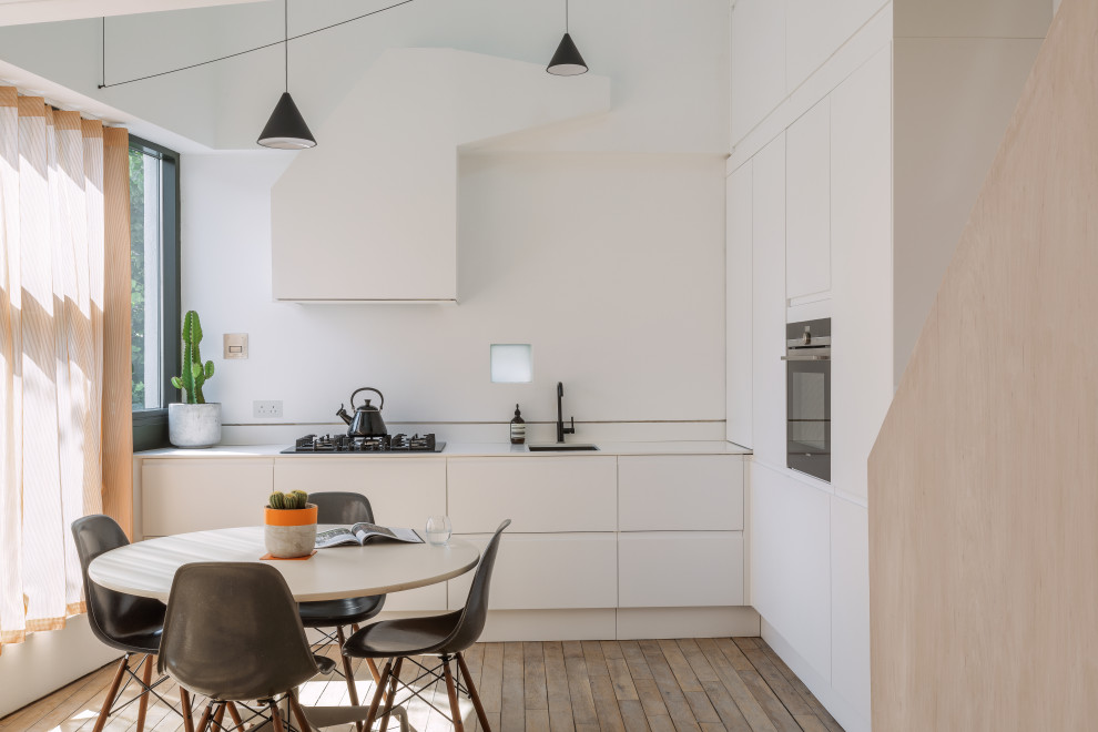 Inspiration for a contemporary l-shaped eat-in kitchen in London with an undermount sink, flat-panel cabinets, white cabinets, stainless steel appliances, dark hardwood floors, no island, brown floor and white benchtop.