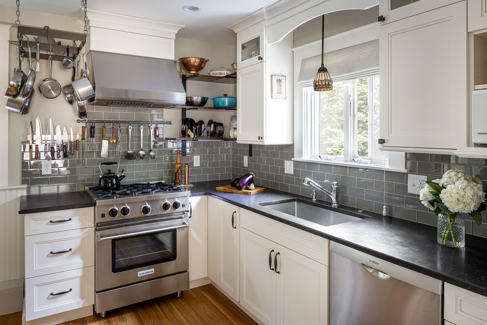 Design ideas for a mid-sized traditional l-shaped separate kitchen in Boston with an undermount sink, flat-panel cabinets, white cabinets, quartz benchtops, green splashback, glass tile splashback, stainless steel appliances, medium hardwood floors, no island, brown floor and black benchtop.