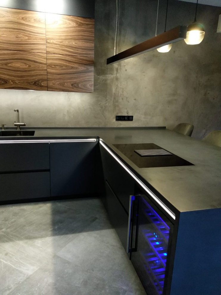 This is an example of a large industrial u-shaped eat-in kitchen in Other with an integrated sink, flat-panel cabinets, dark wood cabinets, solid surface benchtops, grey splashback, porcelain splashback, black appliances, ceramic floors, a peninsula and black benchtop.