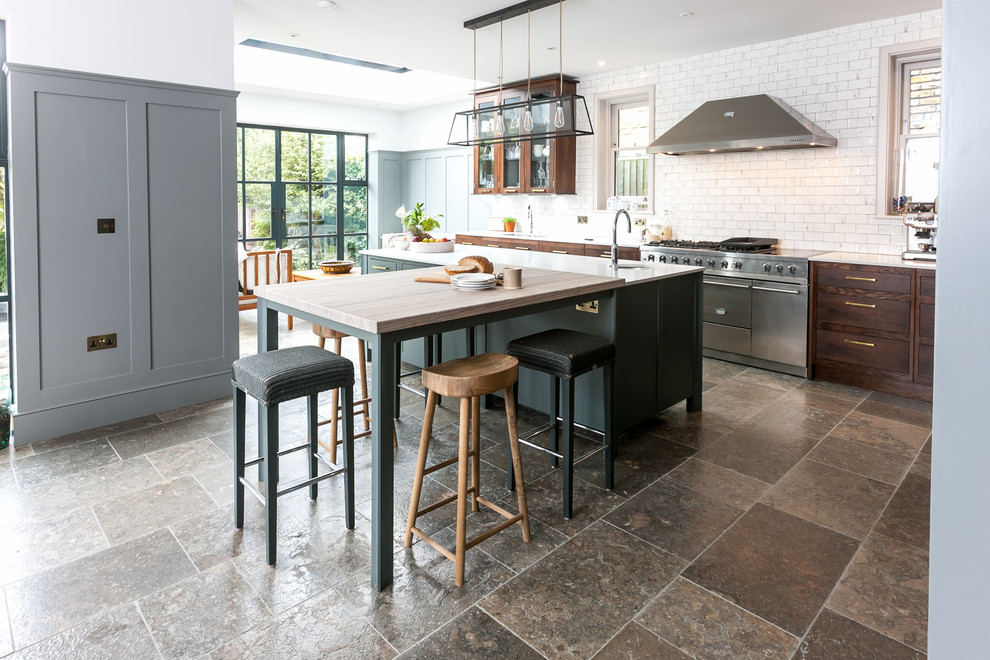 This is an example of a transitional kitchen in London with an undermount sink, dark wood cabinets, white splashback, subway tile splashback, stainless steel appliances, multiple islands and brown floor.