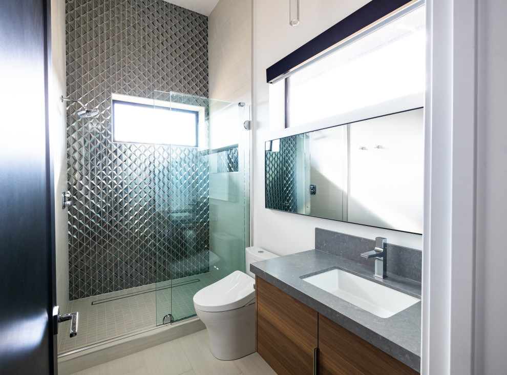 Photo of a medium sized modern shower room bathroom with flat-panel cabinets, medium wood cabinets, a bidet, grey tiles, glass tiles, white walls, porcelain flooring, a submerged sink, engineered stone worktops, beige floors, a sliding door, grey worktops, a single sink and a floating vanity unit.