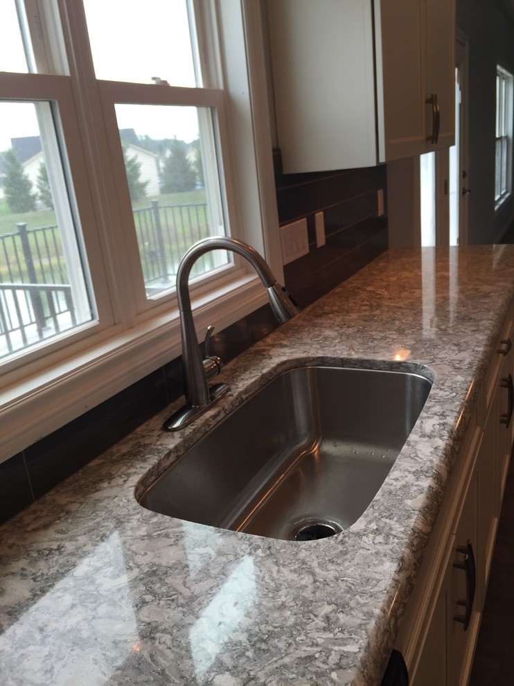 Open concept kitchen - large transitional l-shaped open concept kitchen idea with an undermount sink, raised-panel cabinets, white cabinets, quartz countertops, gray backsplash, stainless steel appliances and an island