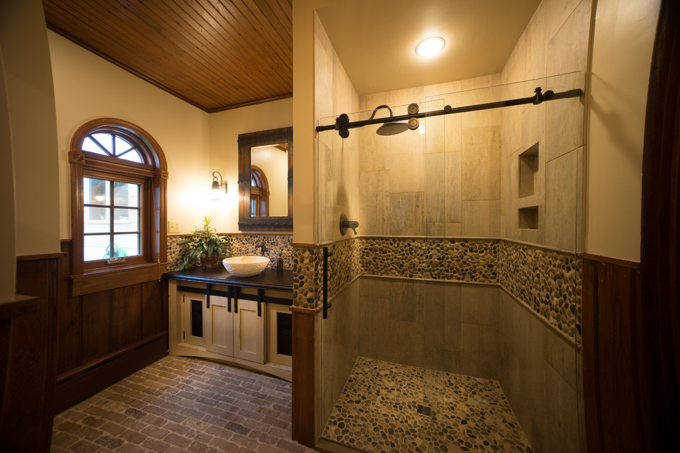 Inspiration for a mid-sized country bathroom in Other with shaker cabinets, beige cabinets, an alcove shower, multi-coloured tile, pebble tile, beige walls, brick floors, a vessel sink, concrete benchtops, multi-coloured floor and a sliding shower screen.