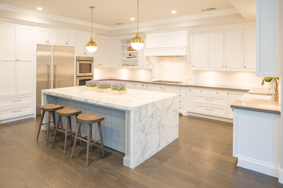 Inspiration for a mid-sized transitional u-shaped eat-in kitchen in Sacramento with a farmhouse sink, shaker cabinets, white cabinets, marble benchtops, white splashback, ceramic splashback, stainless steel appliances, medium hardwood floors, with island and white benchtop.