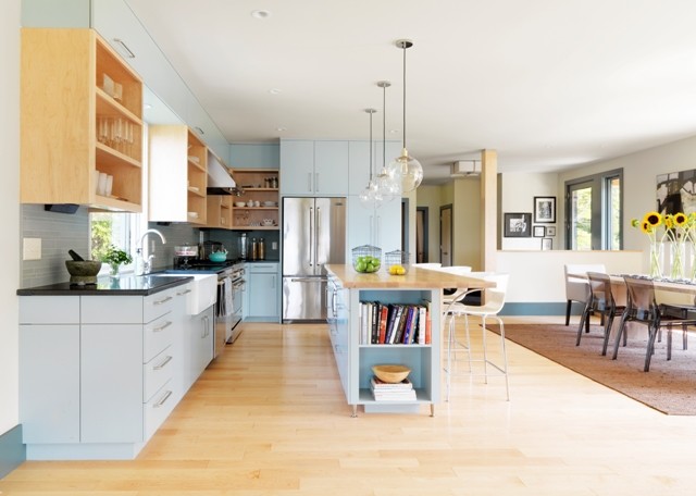 This is an example of a mid-sized contemporary l-shaped open plan kitchen in Burlington with a farmhouse sink, flat-panel cabinets, turquoise cabinets, granite benchtops, green splashback, glass tile splashback, stainless steel appliances, light hardwood floors and with island.