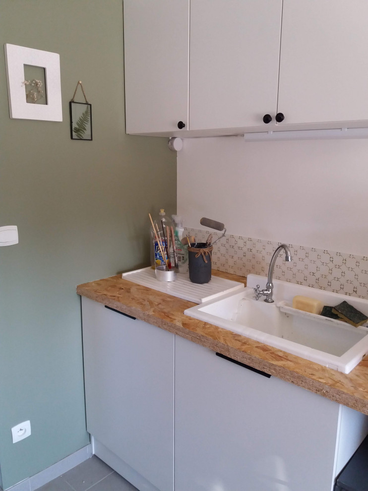Photo of a mid-sized scandinavian l-shaped dedicated laundry room in Other with an undermount sink, wood benchtops, green splashback, green walls, a side-by-side washer and dryer and grey floor.